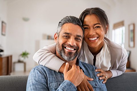 Portrait of multiethnic couple embracing and looking at camera sitting on sofa.