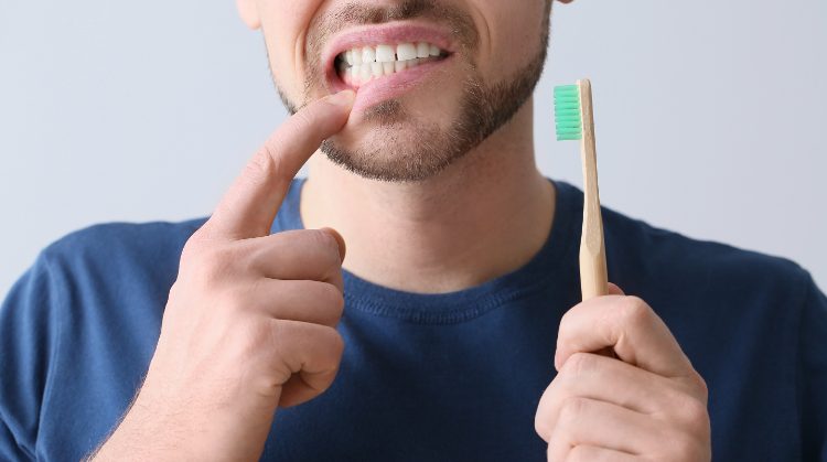 Man pointing to bleeding gums while holding toothbrush – Why Your Gums Bleed.